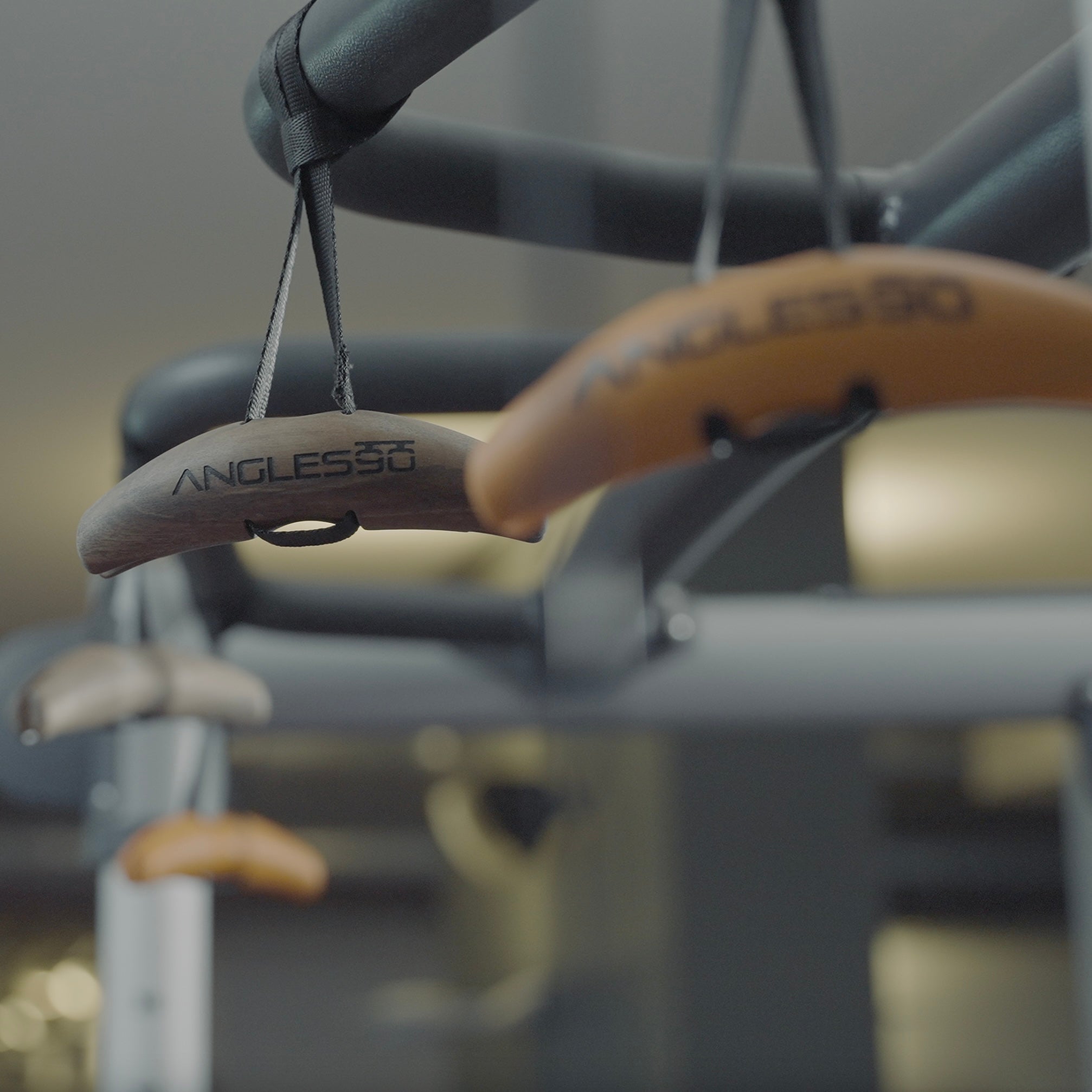 Close-up of sleek, premium walnut hangers with "Angles90 Wood (Limited Edition)" engraved, dangling in an elegant, modern closet setting.